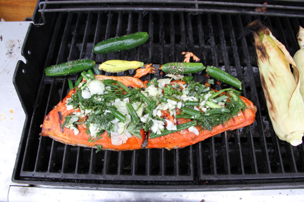 A fillet of red salmon cooking on the barbecue covered in fresh herbs. 