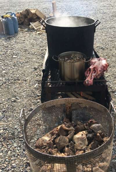 pots boiling over an outdoor fire next to a moose skull and a colander of bones.