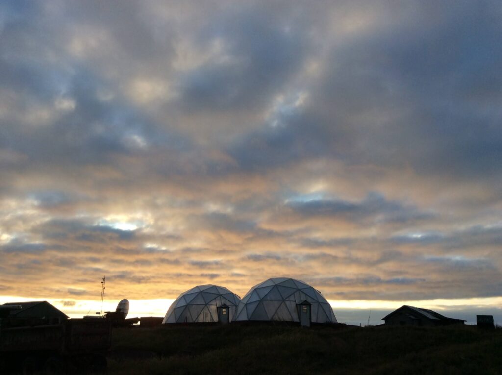 two geodesic dome greenhouses with cloudy sky.