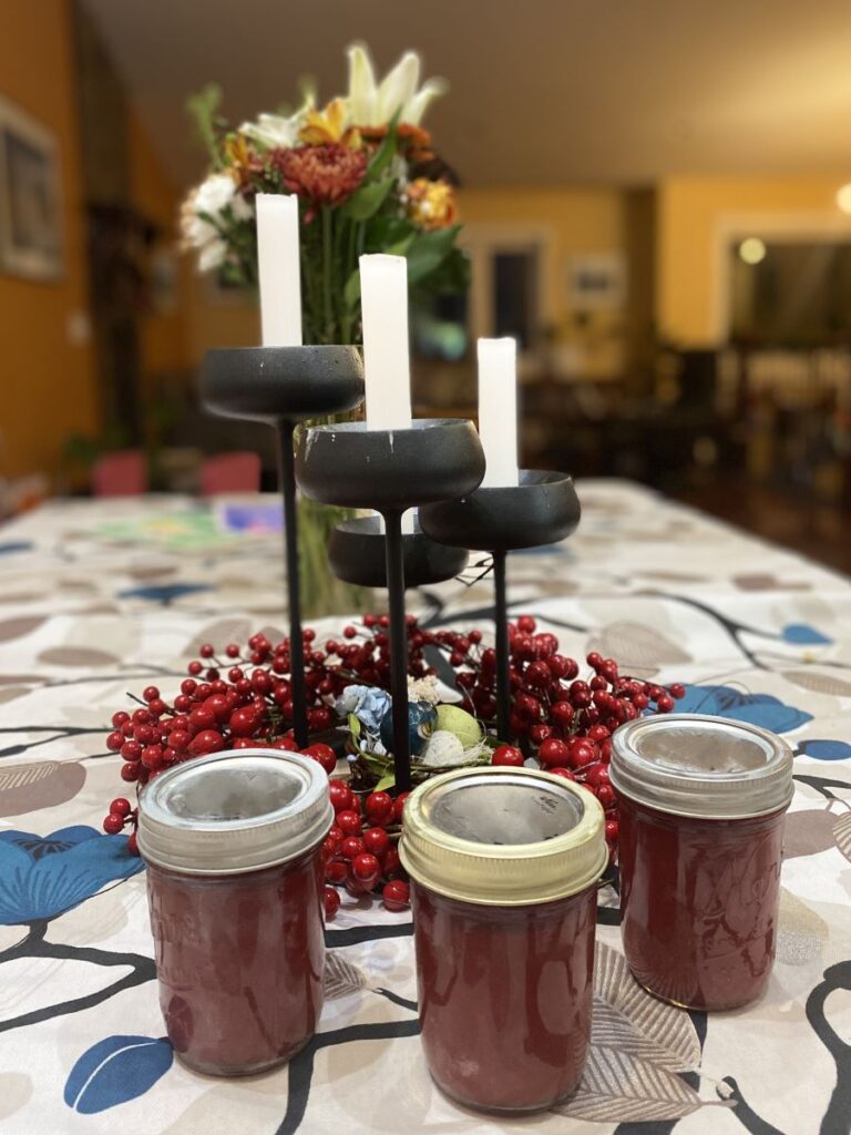 three jars of red syrup with candles in background and red berry wreath